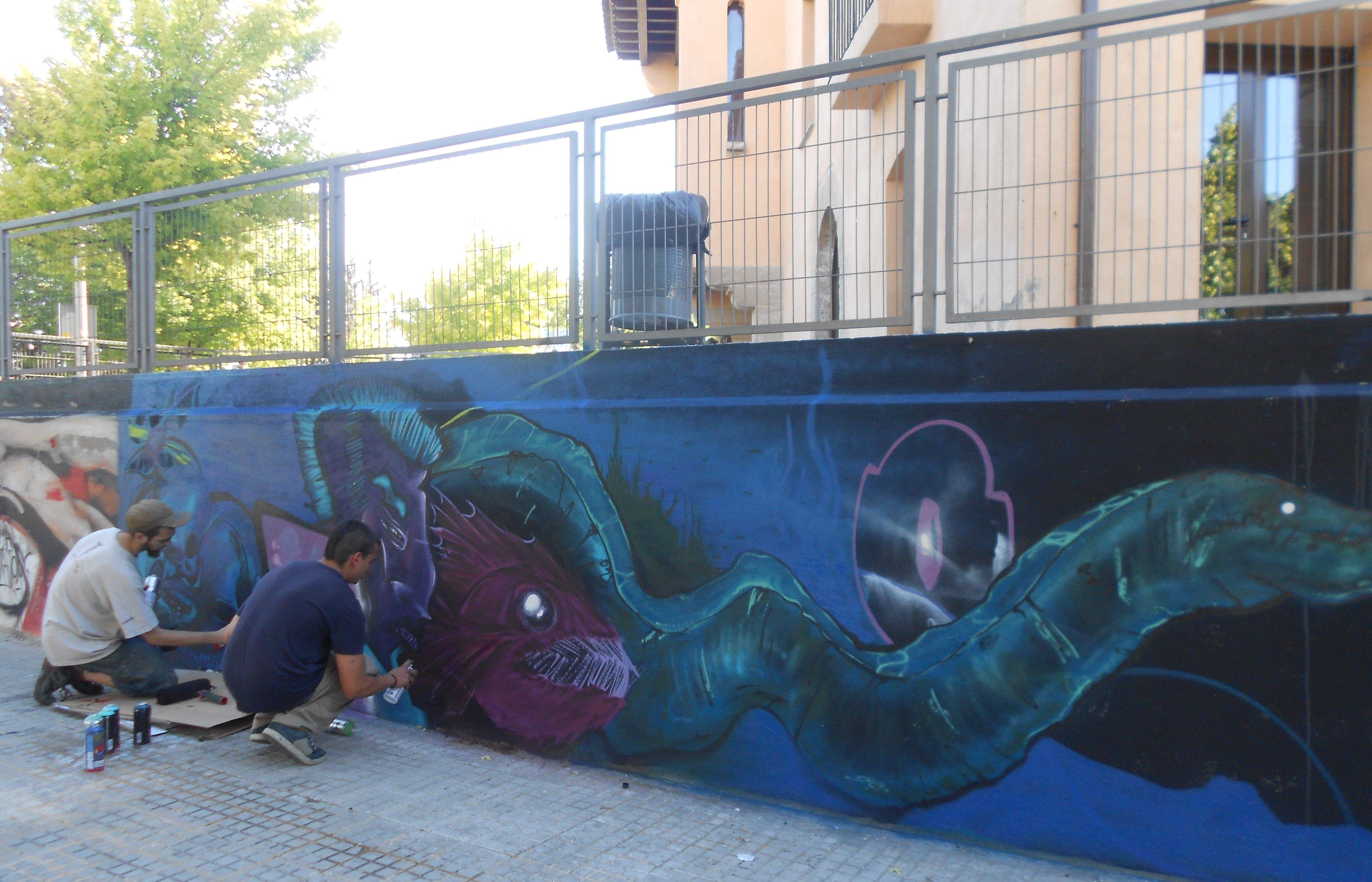 Dos pintors d'art mural treballant sobre l'obra col·lectiva que s'ha exposat aquest 15 de juny. FOTO: Alba Guerrero