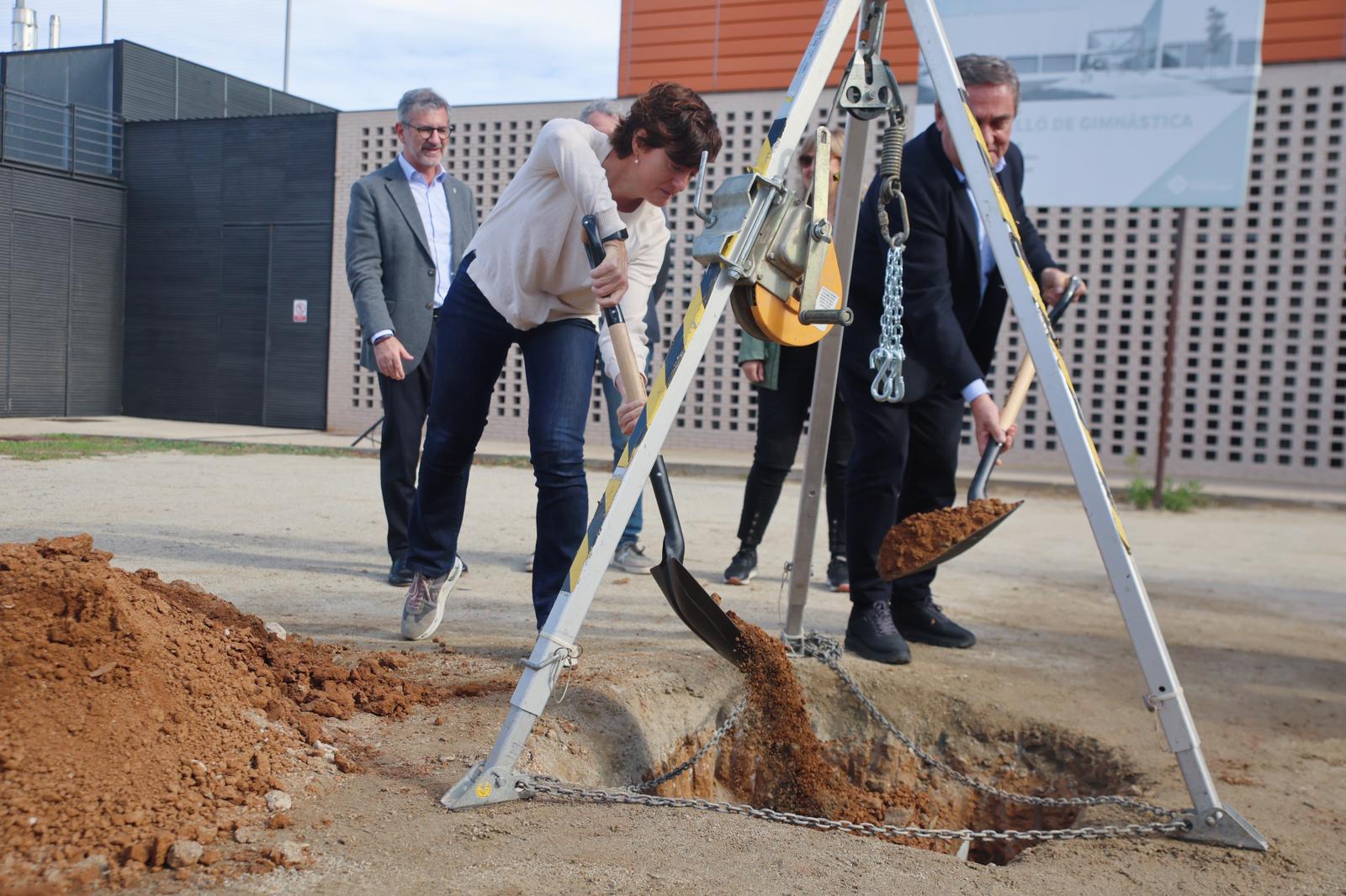 La regidora d'Esports de l'Ajuntament, Núria Escamilla, i el gerent de l'AMB, Ramon Torra, ajundant a enterrar la primera pedra del nou pavelló d'entrenament de gimnàstica a la Guinardera. FOTO: Ajuntament