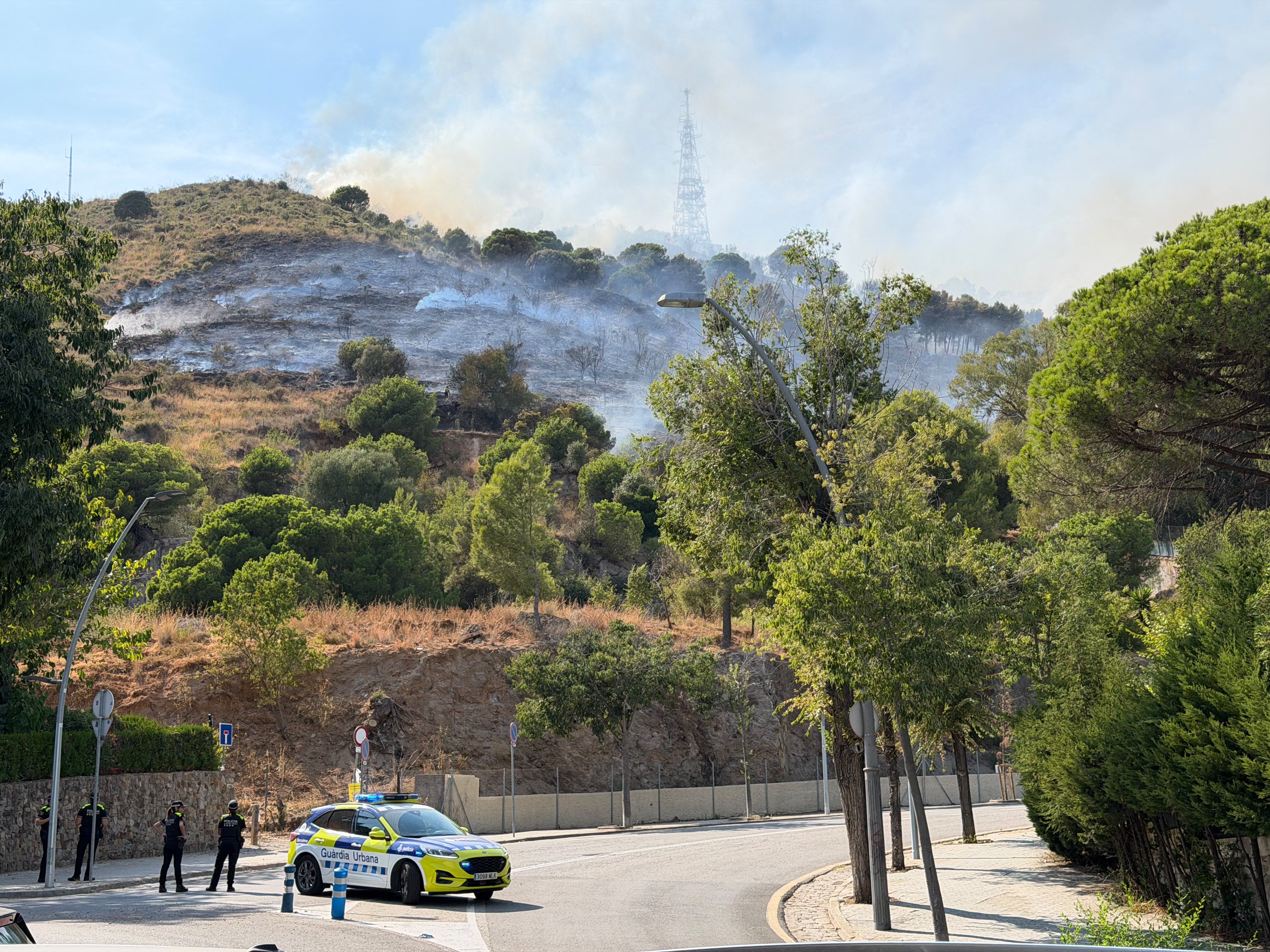 Imatge de l'incendi a Collserola, amb un cotxe de la Guàrdia Urbana barrant el pas FOTO: ACN